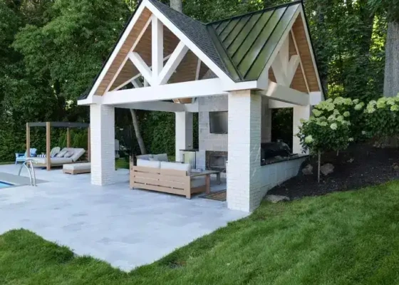 Poolside pavilion with outdoor seating and fire pit in a lush backyard.