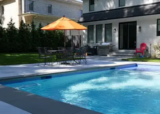 Inground pool with outdoor dining area and umbrella in Long Island backyard.