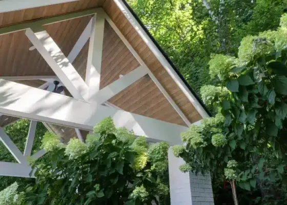Modern outdoor structure with white beams and wooden roof in lush greenery.