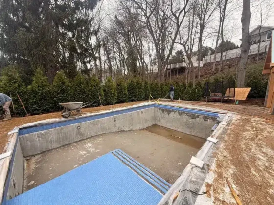 Inground pool under construction with concrete shell and surrounding yard.