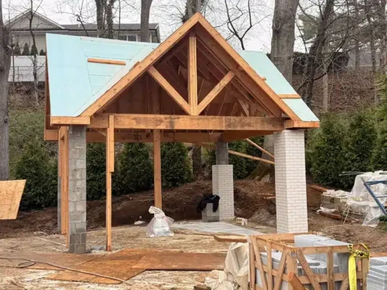 Under construction pool house with wooden framework and roof in progress.