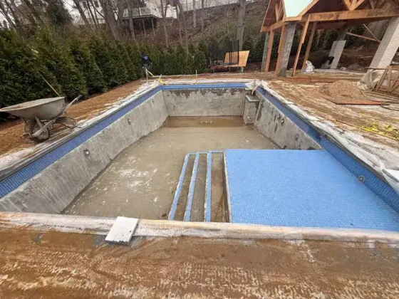 Inground pool under construction with blue safety cover and surrounding deck.