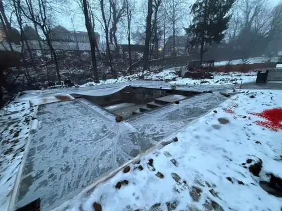 Construction site of an inground pool in winter with snow and trees.