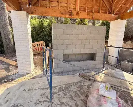 Under construction outdoor pool area with brick fireplace and wooden roof.