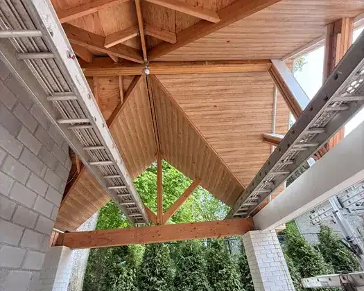 Under construction wooden porch with detailed roof structure and support beams.