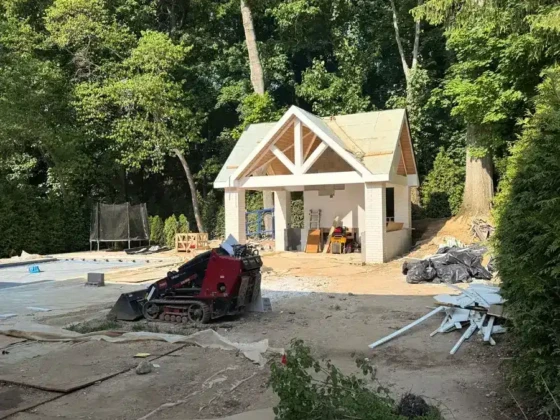 Construction site of a pool house with a small excavator and building materials.