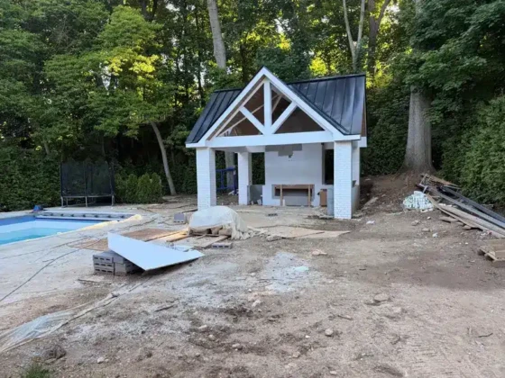 Poolside cabana under construction with surrounding trees and construction materials.