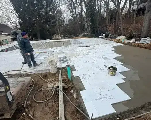 Inground pool construction site with workers and pool shell in progress.