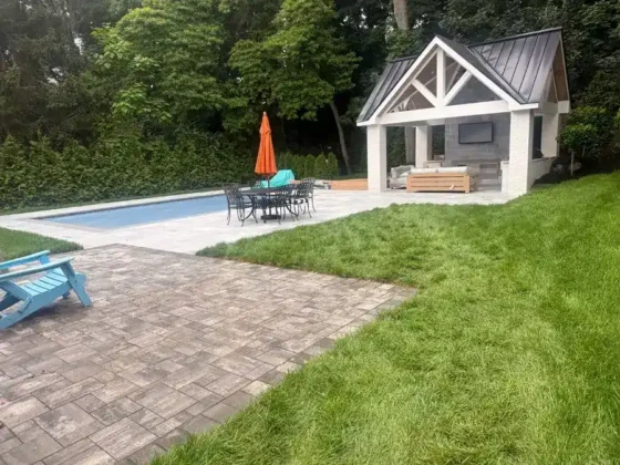 Beautiful backyard with inground pool, outdoor furniture, and pool house in Long Island.