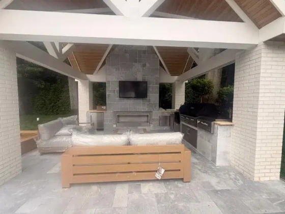 Outdoor kitchen and seating area with fireplace and TV under a pavilion.