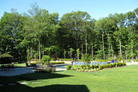 Elegant backyard featuring a pool, outdoor furniture, and lush greenery in Long Island for outdoor living. Beautiful backyard with pool, lush trees, and outdoor furnishings in Long Island.