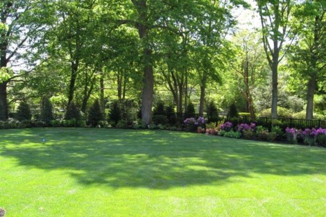 A well-maintained backyard featuring a green lawn, mature trees, and vibrant flower beds, perfect for outdoor activities. Lush green lawn with mature trees and colorful flower beds in a landscaped yard.