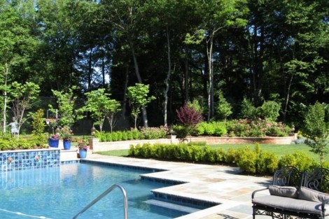 Elegant backyard featuring a custom inground pool, outdoor seating, and vibrant landscaping on Long Island. Beautiful backyard with inground pool, outdoor furniture, and lush greenery.