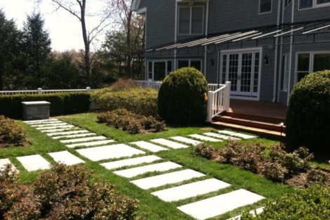 Elegant backyard landscape featuring a stone pathway, trimmed bushes, and a deck for outdoor relaxation. Beautiful backyard landscaping with stone pathway and lush greenery.