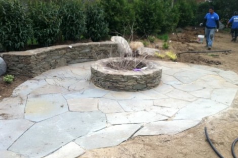 Newly installed stone fire pit with patio area, perfect for outdoor gatherings and relaxation. Stone fire pit with surrounding patio in a landscaped yard.