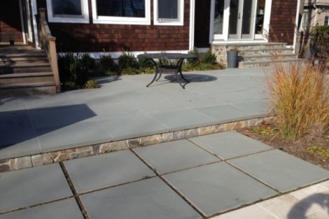 Beautiful outdoor patio with seating area and garden plants, part of a custom landscaping project in Long Island. Concrete patio with outdoor seating and garden plants in Long Island.