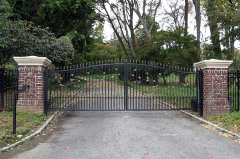 Elegant black wrought iron fence with brick pillars marks the entrance to a lush garden. Black wrought iron fence with brick pillars at driveway entrance.