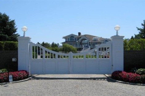 Stylish white driveway gate with decorative elements, leading to a luxurious property in Long Island. White driveway gate with decorative design and landscape background.