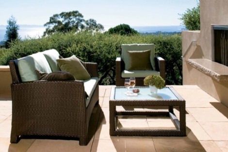 Elegant outdoor living furniture set on patio with view of lush greenery and distant water. Outdoor patio furniture with sofa, chairs, and table overlooking greenery.
