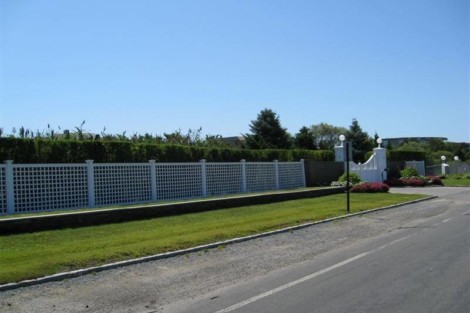 A white lattice fence with outdoor lighting along a well-maintained lawn in Long Island. Long Island fence with lattice design and outdoor lighting.