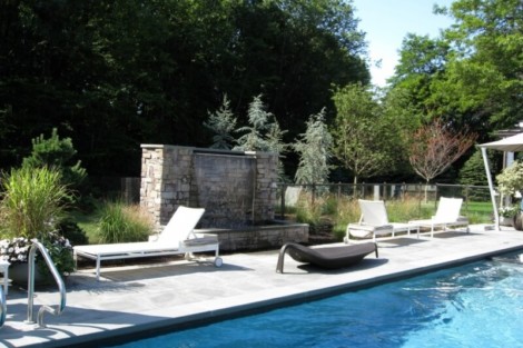 Luxury inground pool with outdoor seating and water feature in a landscaped backyard in Long Island. Beautiful inground pool with outdoor lounge and water feature in Long Island.