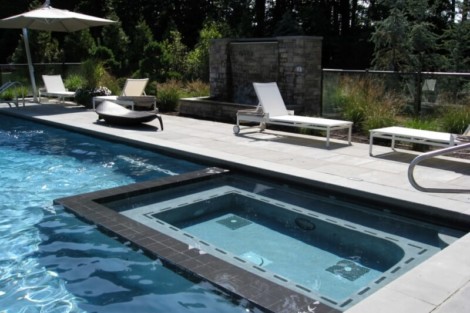 Luxury inground pool with outdoor furniture and lush landscaping in Long Island setting. Inground pool with outdoor lounge chairs and umbrella on Long Island.