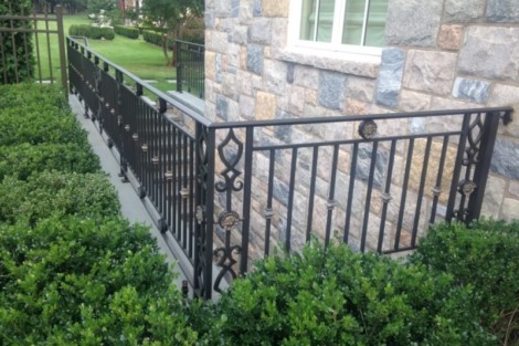 Elegant black metal fence surrounds the inground pool area on Long Island, enhancing safety and aesthetic appeal. Black metal fence around inground pool on Long Island with lush greenery.
