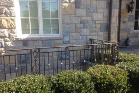 Elegant black metal fence with decorative accents enhances the property’s curb appeal. Durable black metal fence with decorative accents in front of stone house.