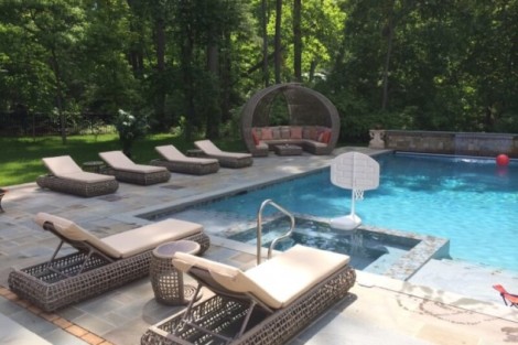 Elegant inground pool with outdoor furniture and lush greenery in Long Island, perfect for outdoor living. Luxury outdoor pool with lounge chairs and seating area in a wooded setting.