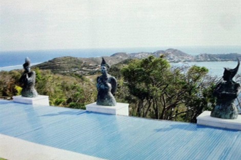 Statues on a terrace overlooking a scenic coastal landscape with hills and water in the background. Outdoor statues overlooking a coastal landscape with hills and water.