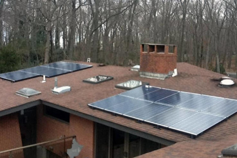 Residential roof with solar panels and vents, surrounded by trees in the background. Solar panels installed on a residential roof with a chimney and vents.