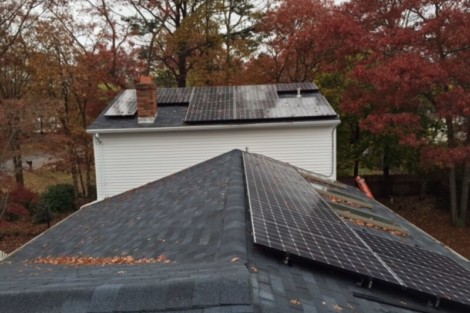 Residential roof equipped with solar panels for renewable energy generation in fall season. Solar panels installed on a house roof with autumn trees in background.