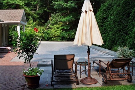 Relaxing outdoor pool area with lounge chairs, umbrella, and lush greenery in Long Island. Inground pool with outdoor furnishings and umbrella in Long Island.