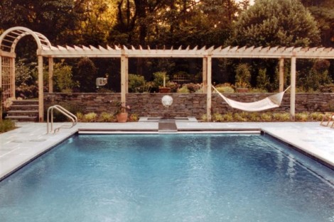 Elegant inground pool with pergola, hammock, and lush greenery in Long Island backyard. Beautiful inground pool with pergola and hammock in outdoor setting.