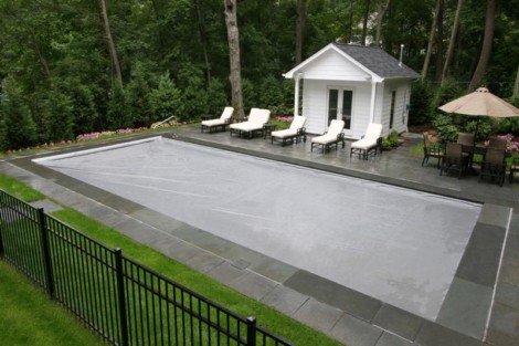 Beautiful inground pool with cover, surrounded by outdoor furniture and a pool house in a lush wooded setting. Inground pool with cover, outdoor furniture, and pool house in wooded area.
