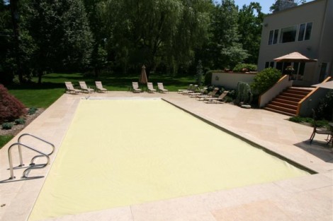 Beautiful Long Island backyard with gunite pool and automatic cover, surrounded by lounge chairs and lush greenery. Gunite pool with automatic cover in a landscaped backyard on Long Island.