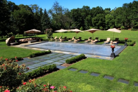 Elegant inground pool with automatic cover, surrounded by lounge chairs and umbrellas in a lush garden setting. Beautiful inground pool with automatic cover and outdoor lounging area.