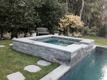 Beautiful inground pool with stone surround, outdoor seating, and lush landscaping in Long Island. Luxury inground pool with stone surround and outdoor furnishings.