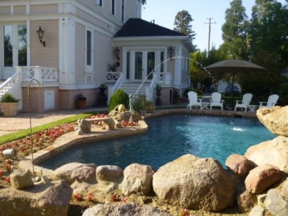 Elegant inground pool with natural rock features and outdoor seating in Long Island backyard. Beautiful inground pool with rocks and outdoor furnishings in Long Island.