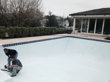 Two workers inspecting the newly renovated inground pool in a residential backyard. Inground pool being renovated with workers inspecting the surface.