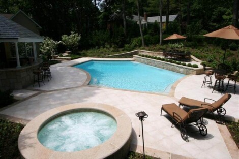 Elegant backyard with inground pool, hot tub, lounge chairs, and shaded seating areas in Long Island. Beautiful inground pool with hot tub and outdoor furnishings in a lush backyard.