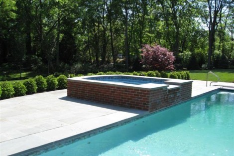 Luxury inground pool with hot tub and outdoor seating area in a lush backyard setting. Beautiful inground pool with hot tub and outdoor furnishings in Long Island.