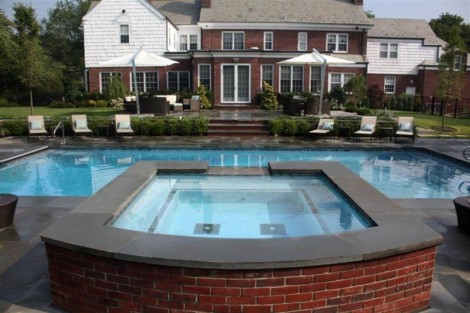 Luxury outdoor pool with hot tub and lounge chairs in a spacious backyard setting. Beautiful inground pool with hot tub and outdoor seating area in Long Island.