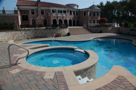 Beautiful inground pool with hot tub and outdoor seating area in a luxurious backyard setting. Elegant inground pool with hot tub and outdoor furnishings on Long Island.