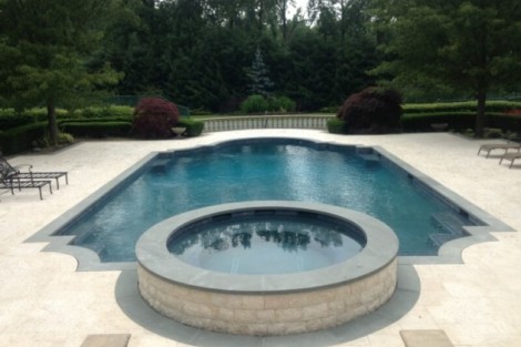 Elegant inground pool with hot tub, surrounded by greenery and outdoor furnishings on Long Island. Beautiful inground pool with attached hot tub in a lush backyard setting.