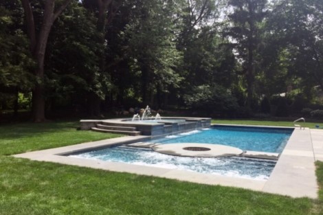 Custom inground pool with spa, waterfall, and surrounding lush greenery in Long Island. Beautiful inground pool with spa and waterfall in a lush backyard.