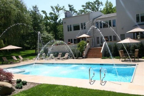 Beautiful inground pool with water features, surrounded by outdoor furniture and lush greenery in Long Island. Inground pool with water fountains and outdoor seating on Long Island.