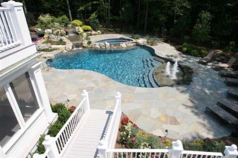 Elegant inground pool with hot tub and surrounding outdoor furnishings in a lush garden setting. Beautiful inground pool with hot tub and outdoor seating on Long Island.