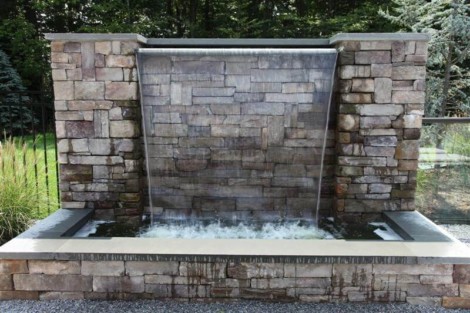 Elegant stone water fountain with waterfall enhances outdoor living space in Long Island. Stone water fountain with waterfall for outdoor landscape design.