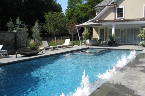 Luxury inground pool with water features and outdoor furniture in a scenic Long Island backyard. Inground pool with water jets and outdoor lounging area in Long Island.
